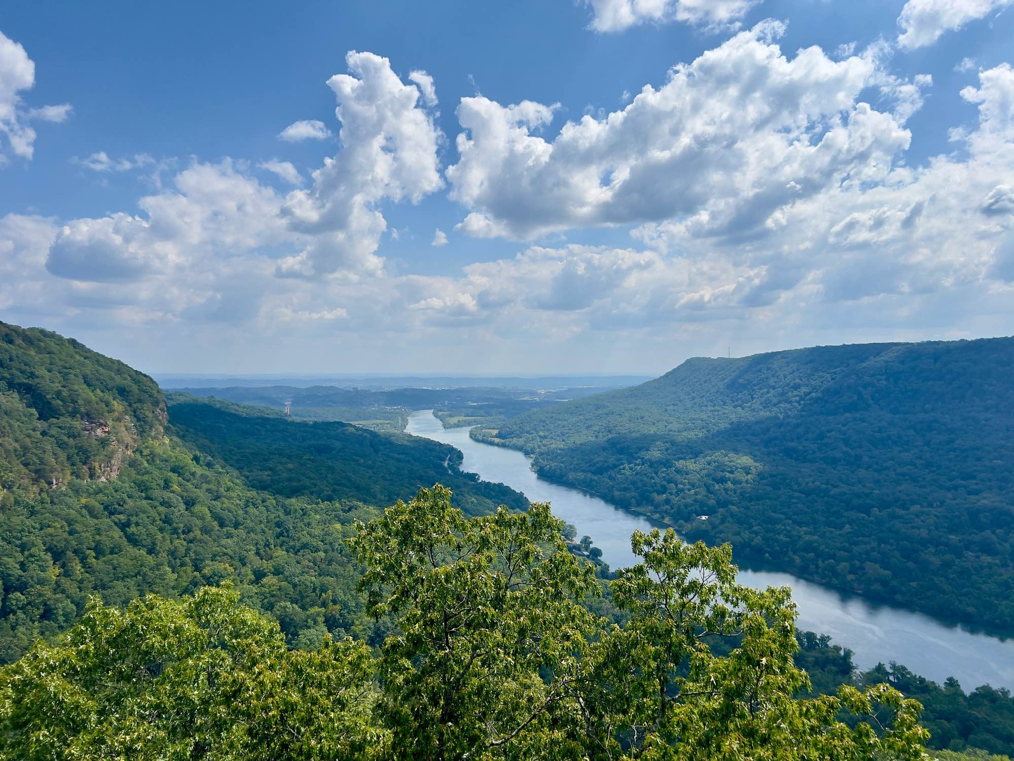 Overlook view of the Tennessee River winding between tree-covered ridges of the Tennessee Valley near Hixson, TN under a partly cloudy summer sky.